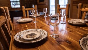 A wooden dining table set with plates and wine glasses, with a sign reading "KAMICHIBI Cabanas Broken Bow".