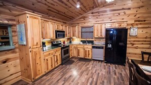 A compact kitchen with wooden cabinets, a microwave, a stove, a dishwasher, and a refrigerator. - Y Knot- Broken Bow/Hochatown- 2bd (Broken Bow)