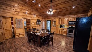 A wooden cabin interior with a dining area, kitchen, and a refrigerator. - Y Knot- Broken Bow/Hochatown- 2bd (Broken Bow)