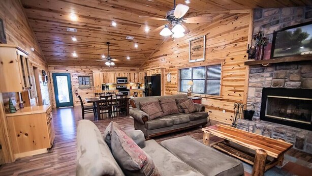 A log cabin interior with a dining area, two sofas, a fireplace, and a kitchen. - Y Knot- Broken Bow/Hochatown- 2bd (Broken Bow)