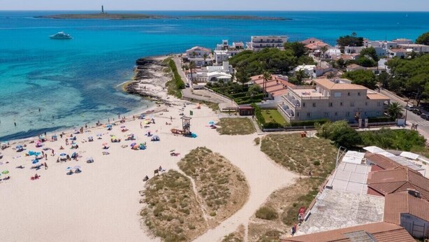 Una cittadina costiera con una spiaggia, edifici e un faro in lontananza.