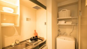 A compact kitchen with a sink, stove, and a small countertop. There is a shelf with folded towels and a basket. - SAKIZO VILLA Kyoto Jingu-michi Sanjo 405 (Kyoto)