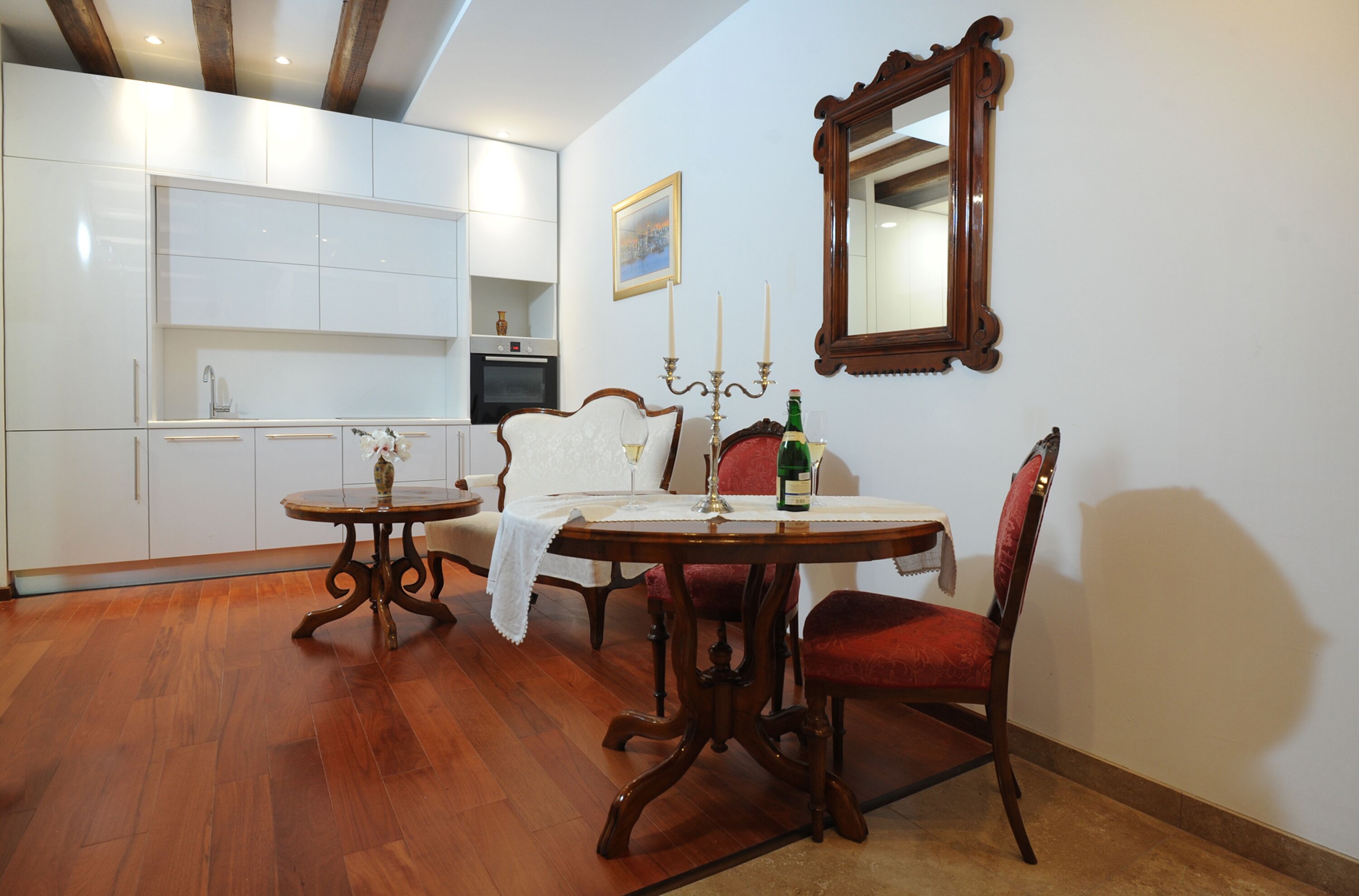 A dining area with a round table, two chairs, a chandelier, and a mirror on the wall.