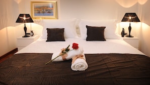 A neatly made bed with a brown bedspread, white pillows, and a single red rose. There are two bedside lamps on white nightstands, and a framed picture on the wall. - Apartments Felicitas (Split)