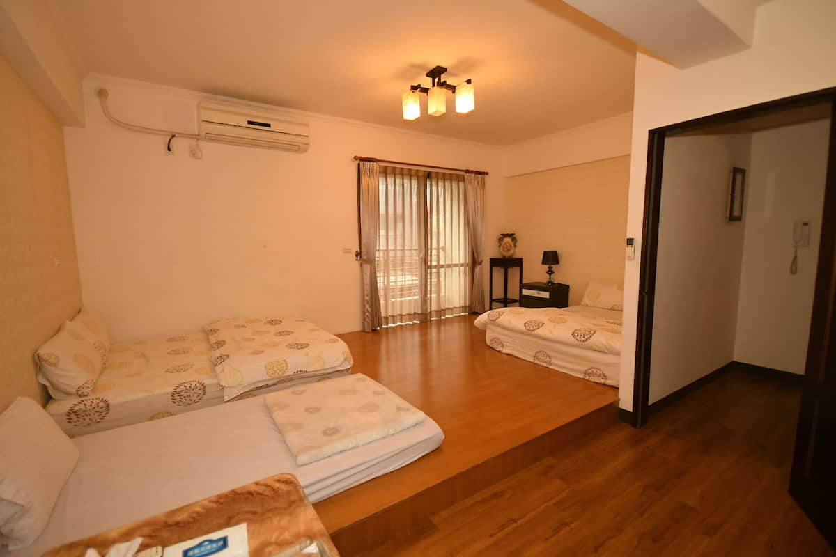 Hotelkamer met twee bedden, een houten vloer, een plafondlamp, een airconditioning en een deur naar een andere kamer.