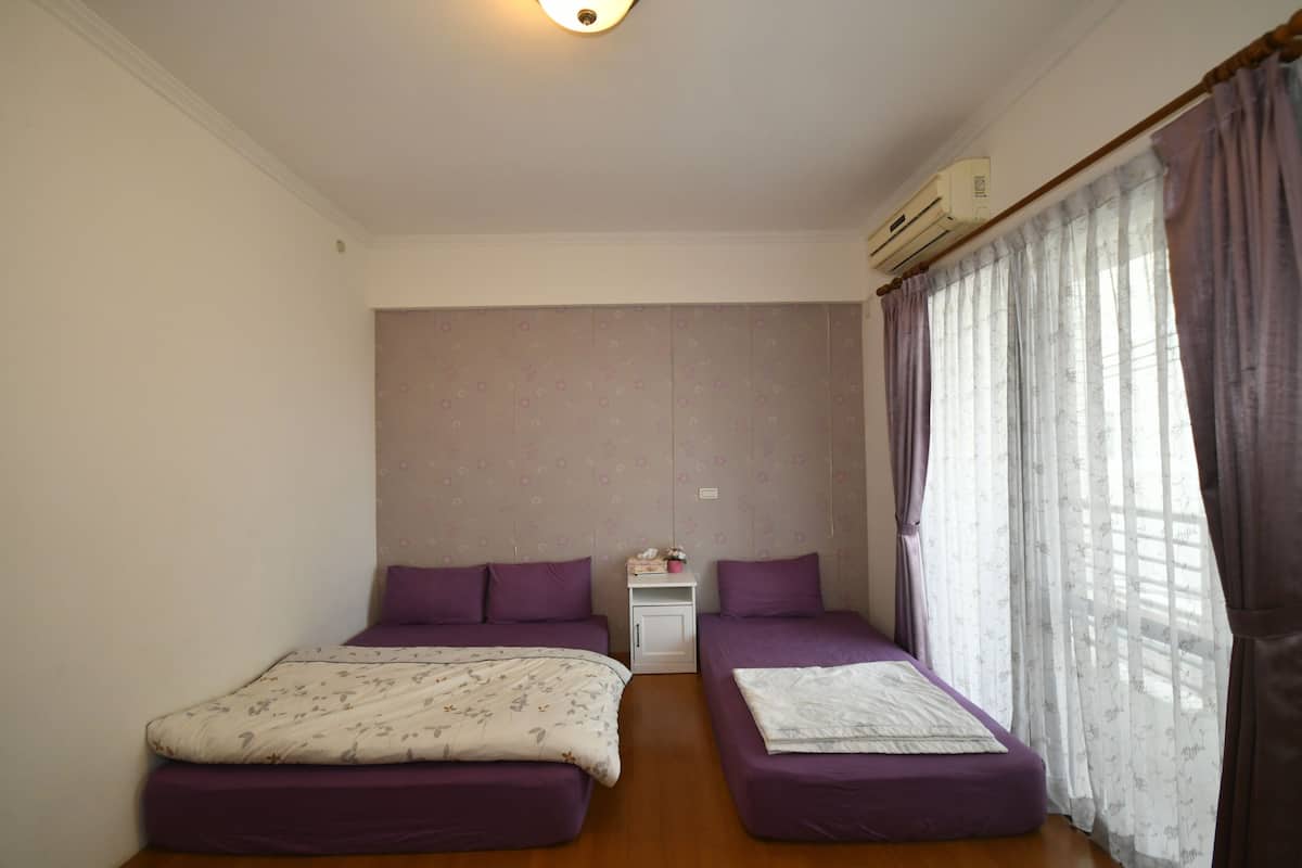 Een kamer met twee bedden, een klein nachtkastje, een airconditioning en een raam met gordijnen.