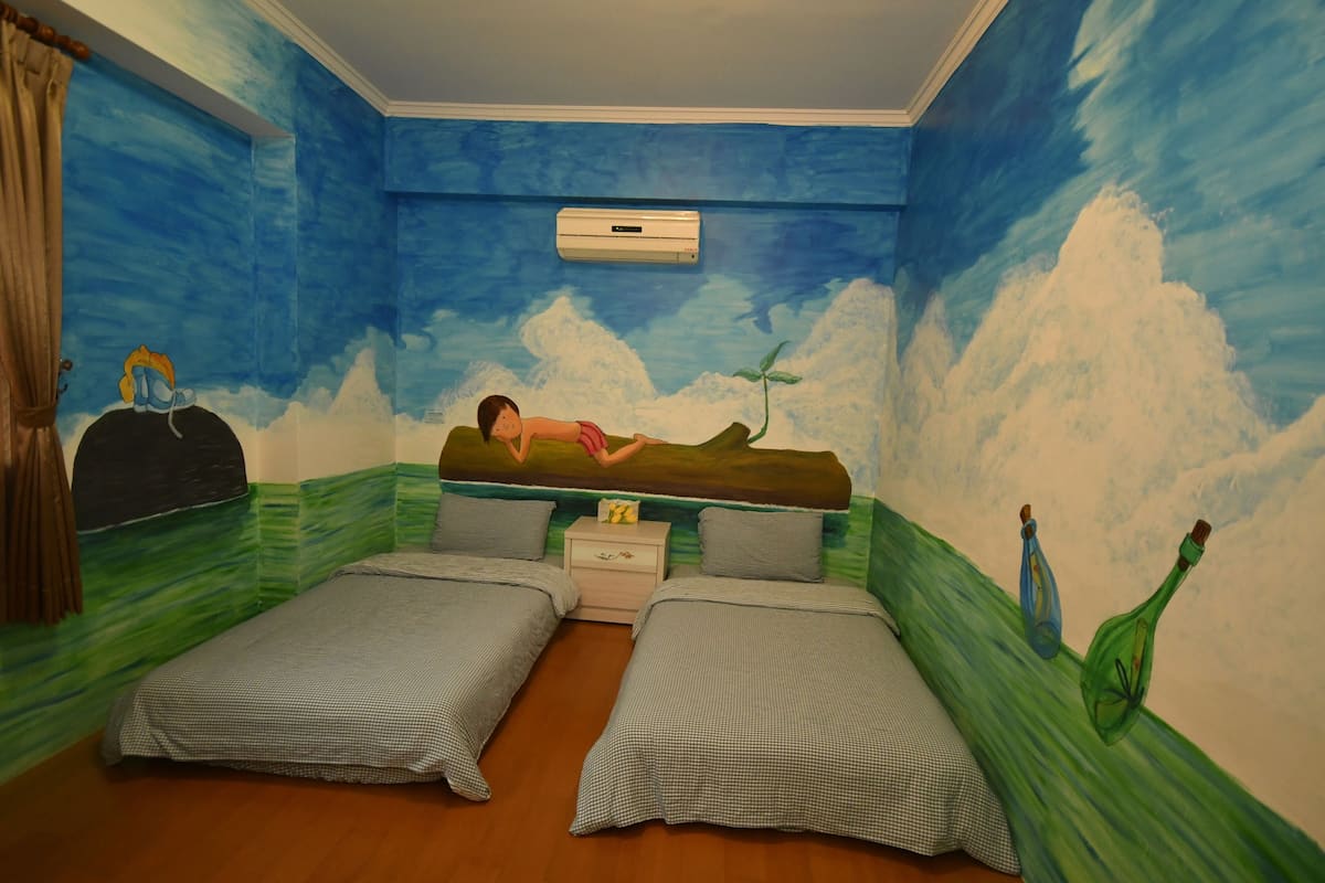 Een kamer met twee bedden, een nachtkastje en een muurschildering van een persoon die in bed ligt.