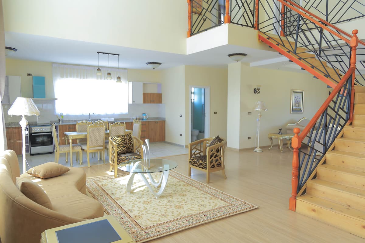 A spacious living area with a dining table, comfortable seating, a staircase, and a kitchen in the background.