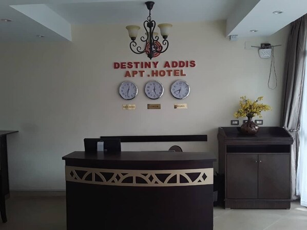 A reception desk with a chandelier, clocks displaying different time zones, and a sign for Destiny Addis APT. HOTEL.