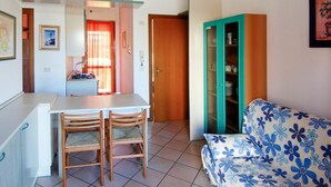 Um espaço de estar compacto com cozinha compacta, área de jantar para duas pessoas, sofá estampado com motivos florais e armário verde-água com portas de vidro.