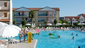 Ein Schwimmbeckenbereich mit Liegestühlen und Sonnenschirmen, umgeben von mehrstöckigen Gebäuden mit Balkonen.