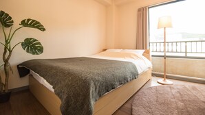 A bedroom with a bed, a potted plant, a floor lamp, and a view of the outside.