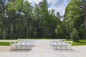 An outdoor seating area with white chairs and tables, surrounded by a forested landscape.