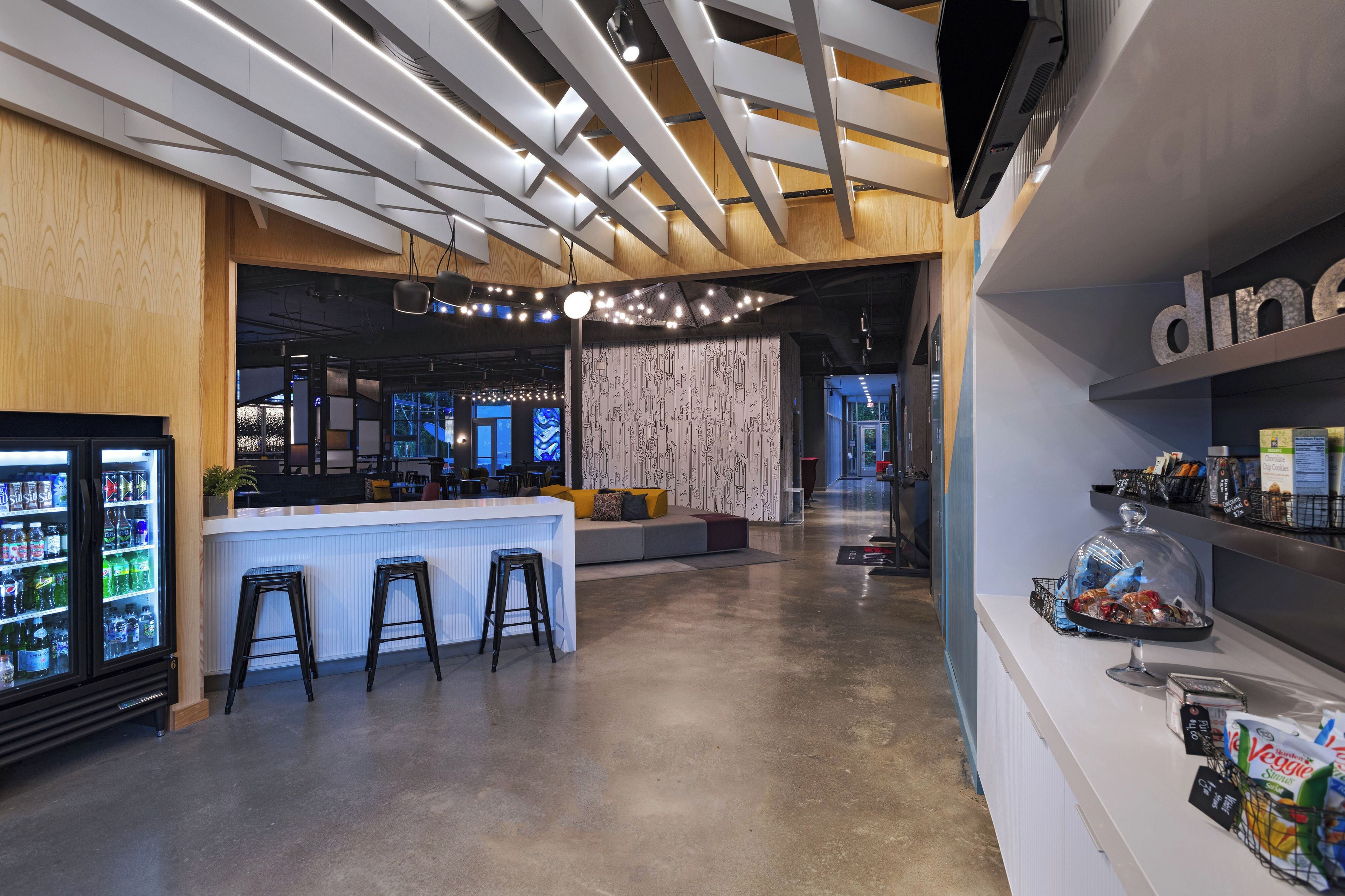 Un área de bar moderna con mostrador, taburetes y refrigerador lleno de bebidas.