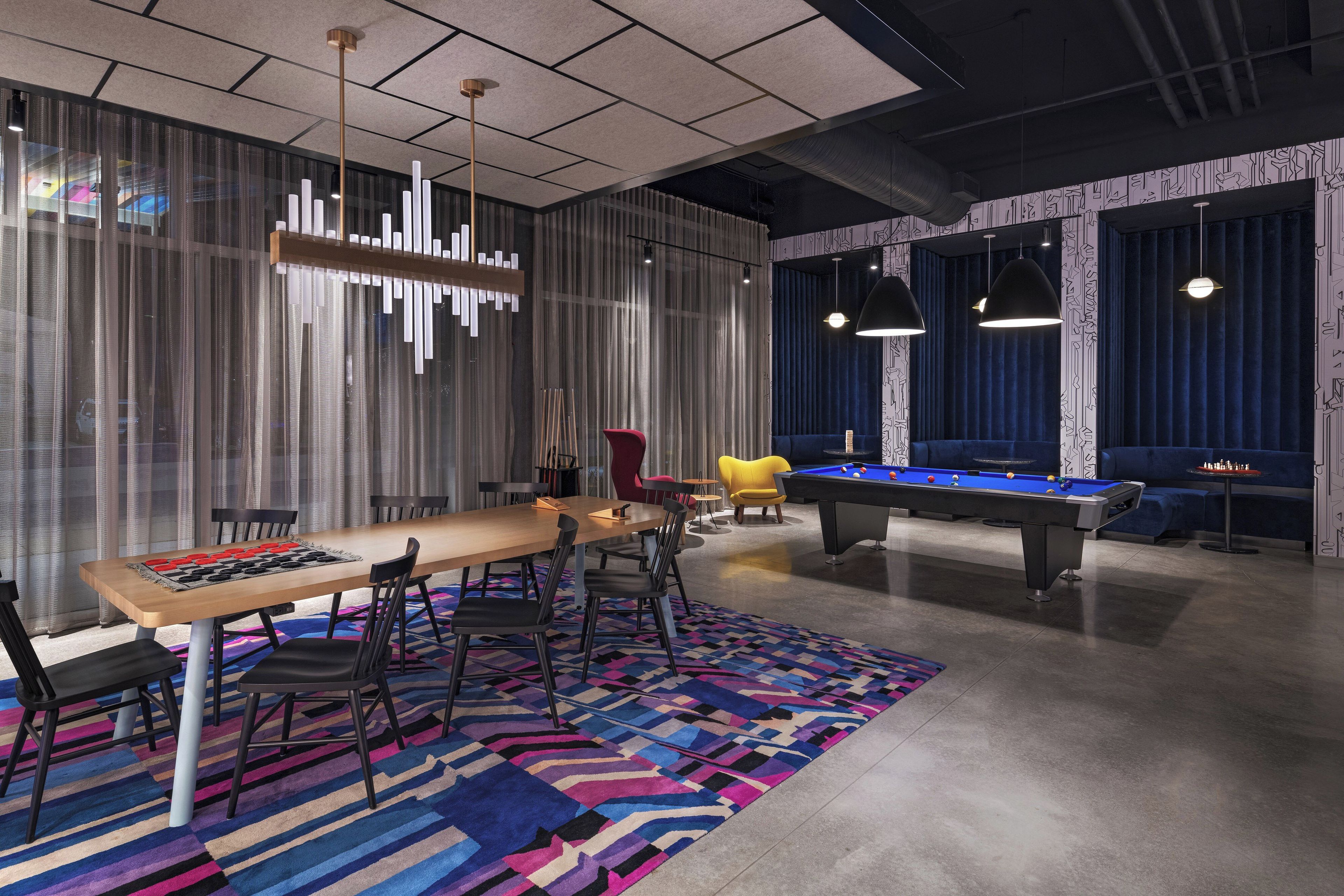 Une pièce moderne équipée d’une table de billard, d’une longue table avec des chaises et d’un tapis aux couleurs vives.