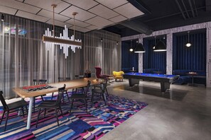 A modern room with a pool table, a long table with chairs, and a colorful rug.