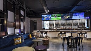 A bar area with multiple screens, seating, and a bar counter. - Aloft by Marriott Little Rock West (Little Rock)