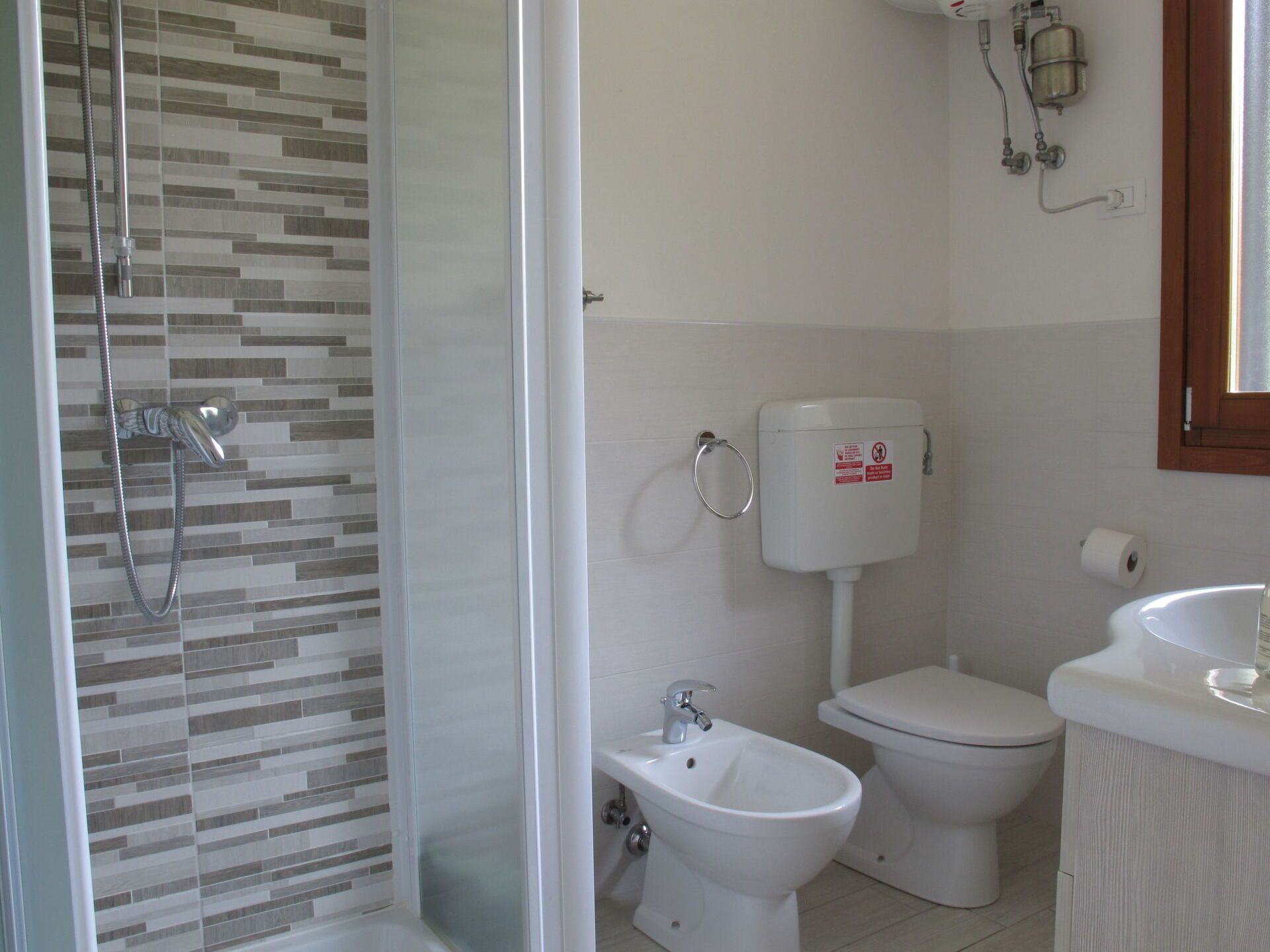 A bathroom with a shower, toilet, bidet, and sink.
