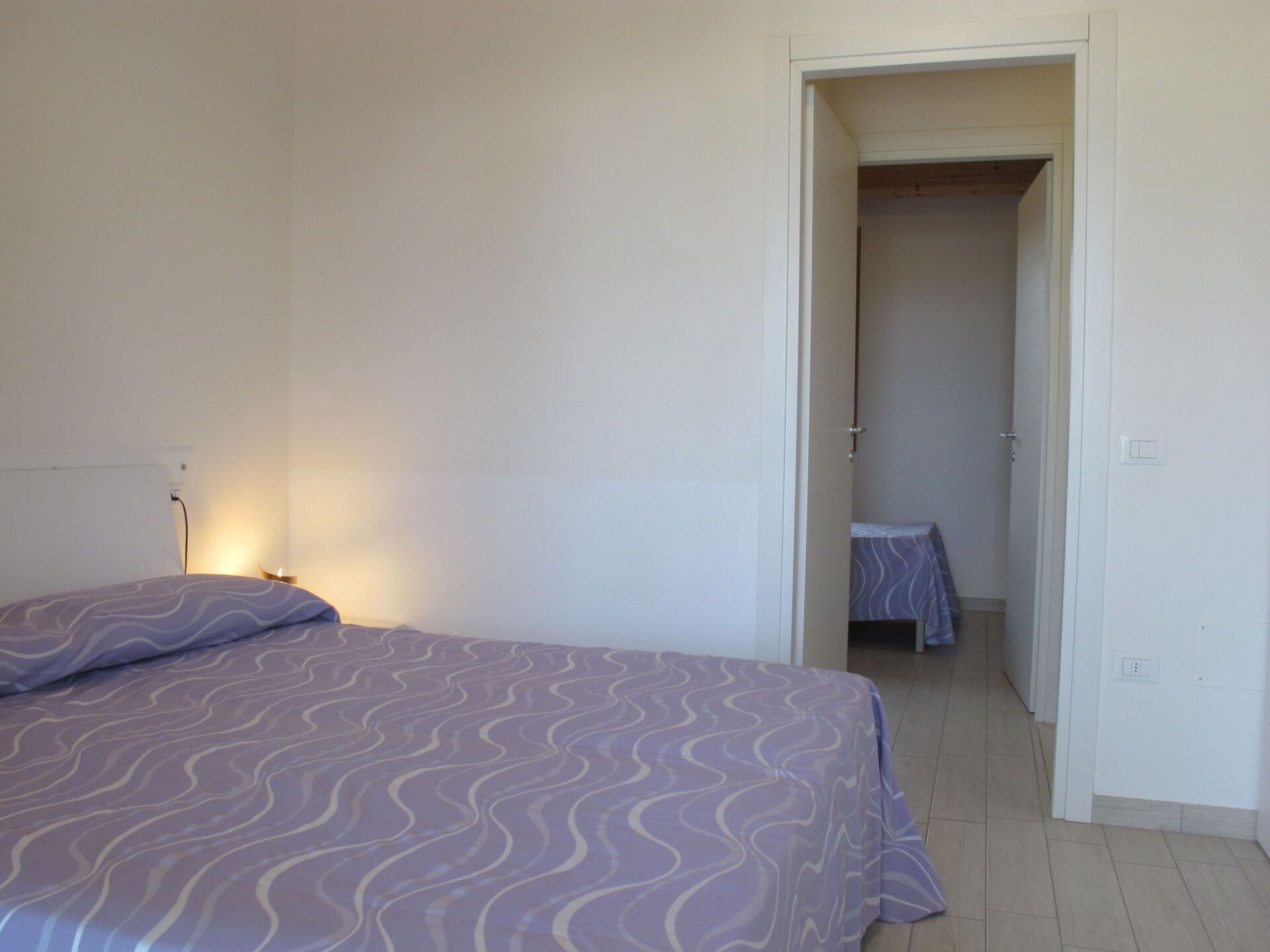 Een slaapkamer met een bed, nachtkastje en een deur naar een badkamer.