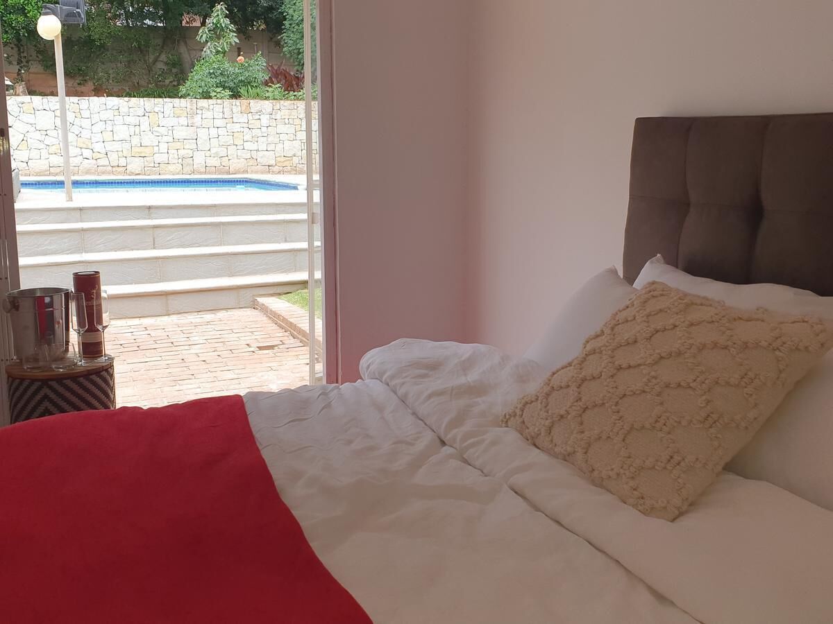 A bedroom with a bed, a view of a swimming pool, and a stone wall outside.