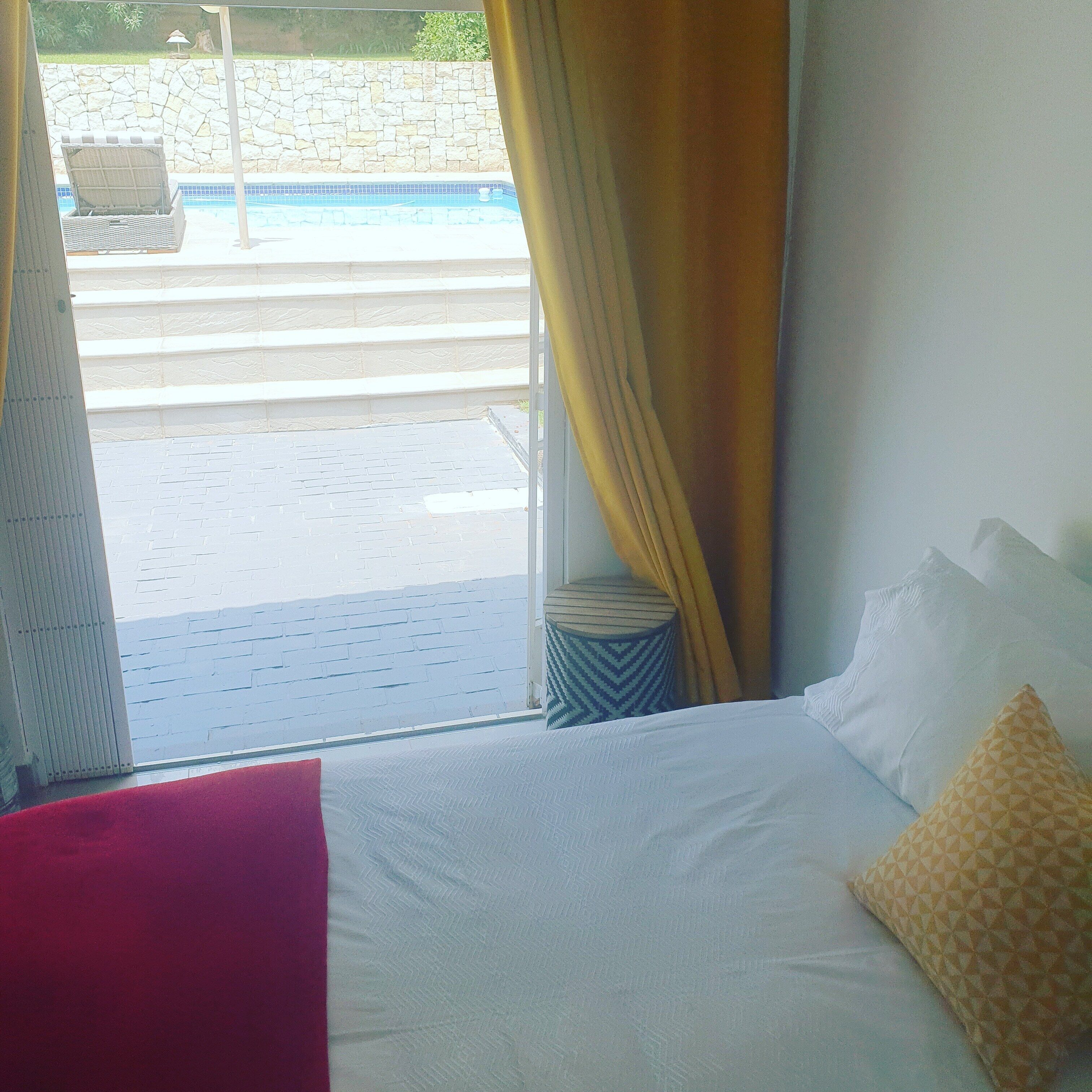 A hotel room with a bed, a window with curtains, and a view of a swimming pool and outdoor area.