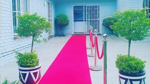 A building with a red carpet leading to the entrance, flanked by potted plants and metal stanchions. - Ouklip Place (Roodepoort)