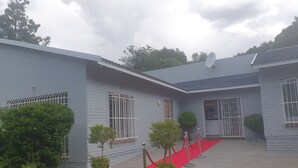 A building with a red carpet leading to the entrance, potted plants, and a satellite dish on the roof. - Ouklip Place (Roodepoort)