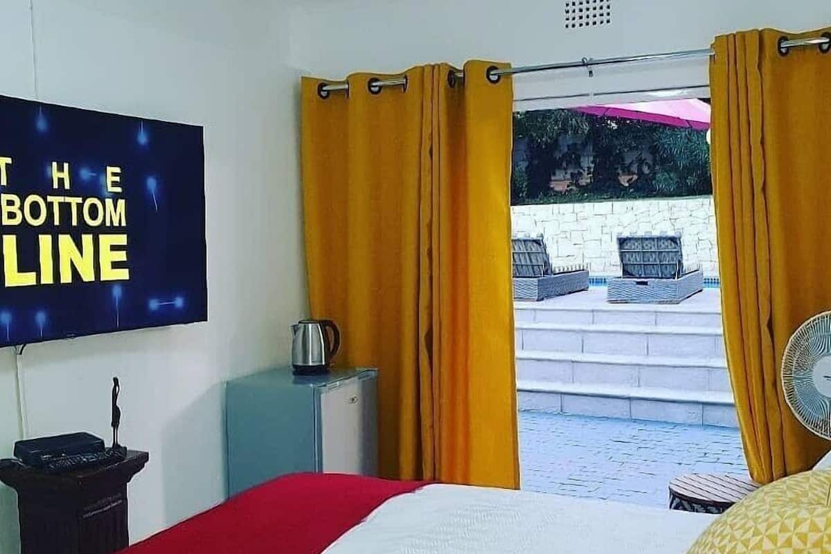 A hotel room with a bed, a TV on the wall, a tray with tea and cups, and a view of the outside.