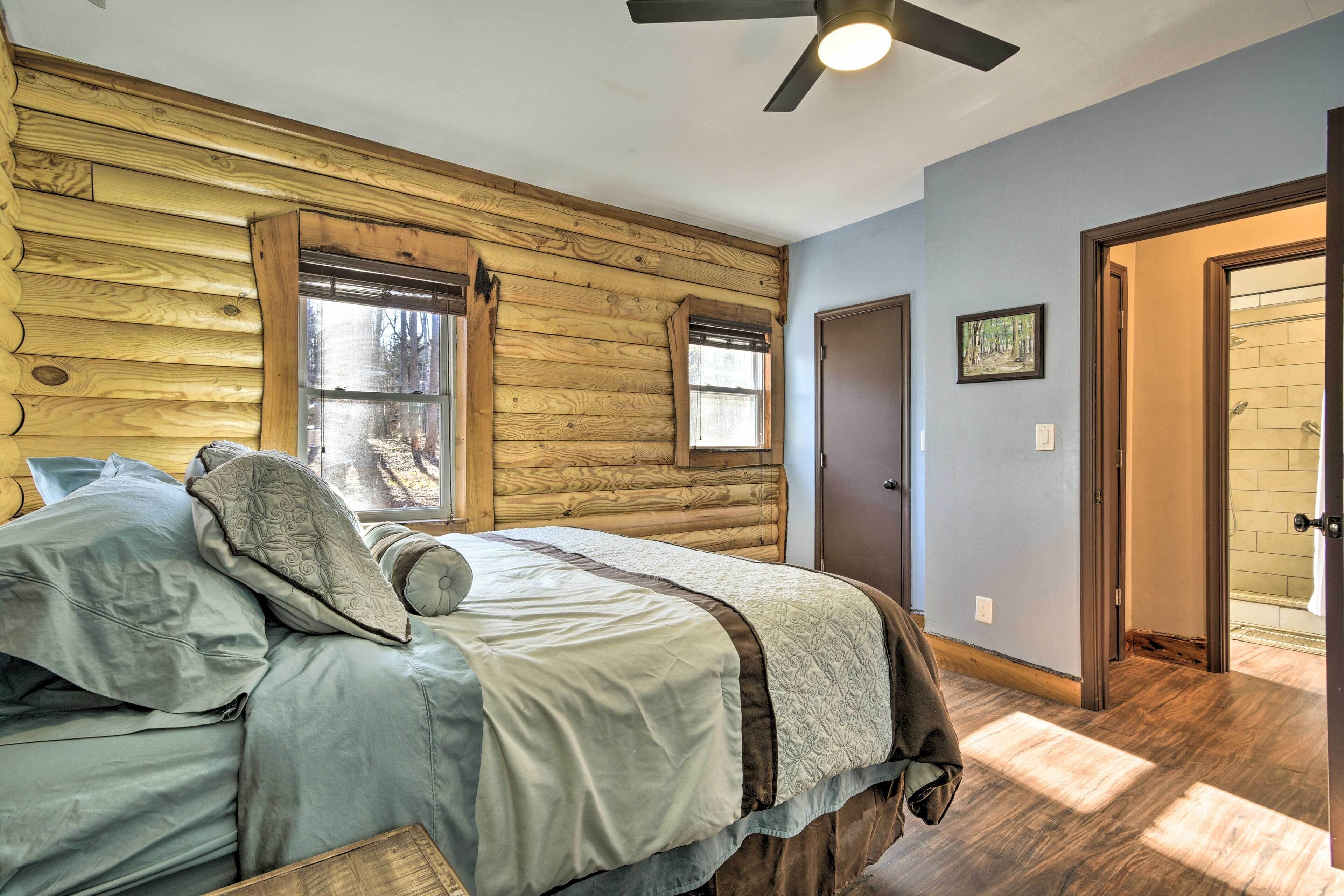 Ein Schlafzimmer in einer Blockhütte mit Bett, Holzwänden, Deckenventilator und Blick ins Freie.