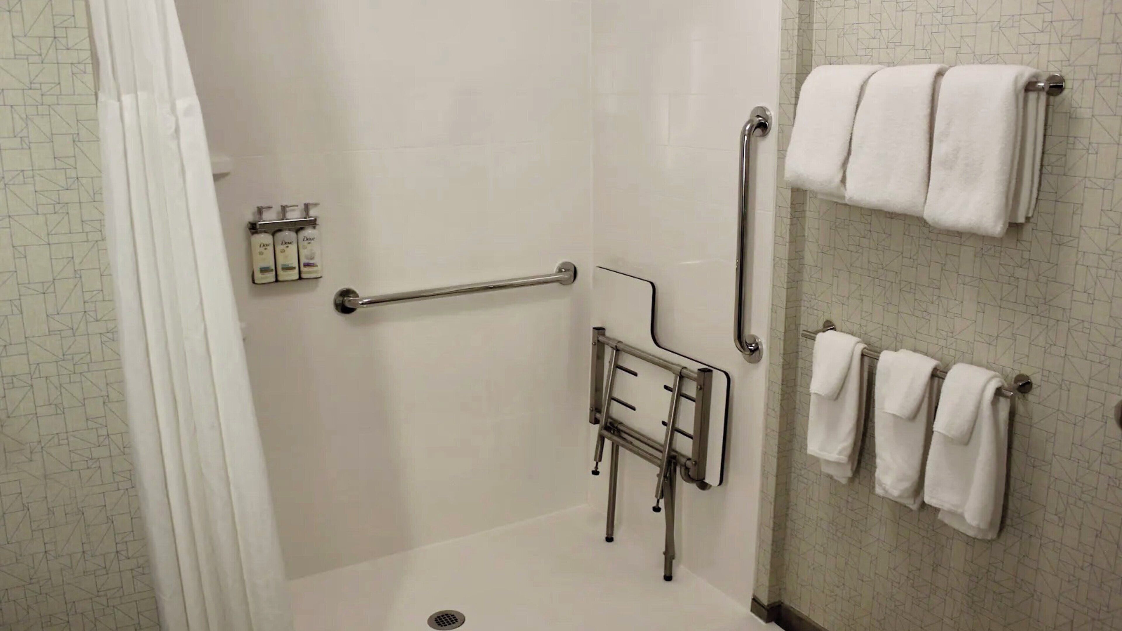 A bathroom with a shower, grab bars, a towel rack, and a toilet with a grab bar.