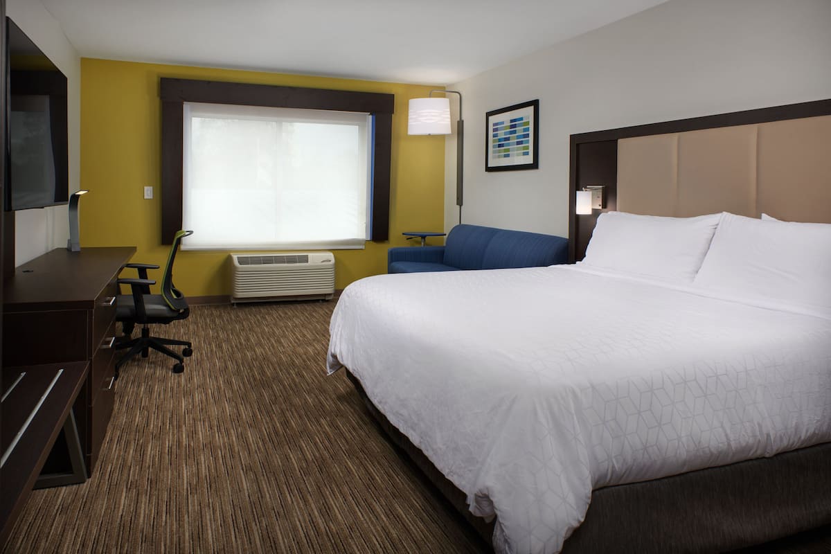 Una habitación de hotel con una cama grande, un escritorio, una silla, un aire acondicionado y una ventana con cortinas.