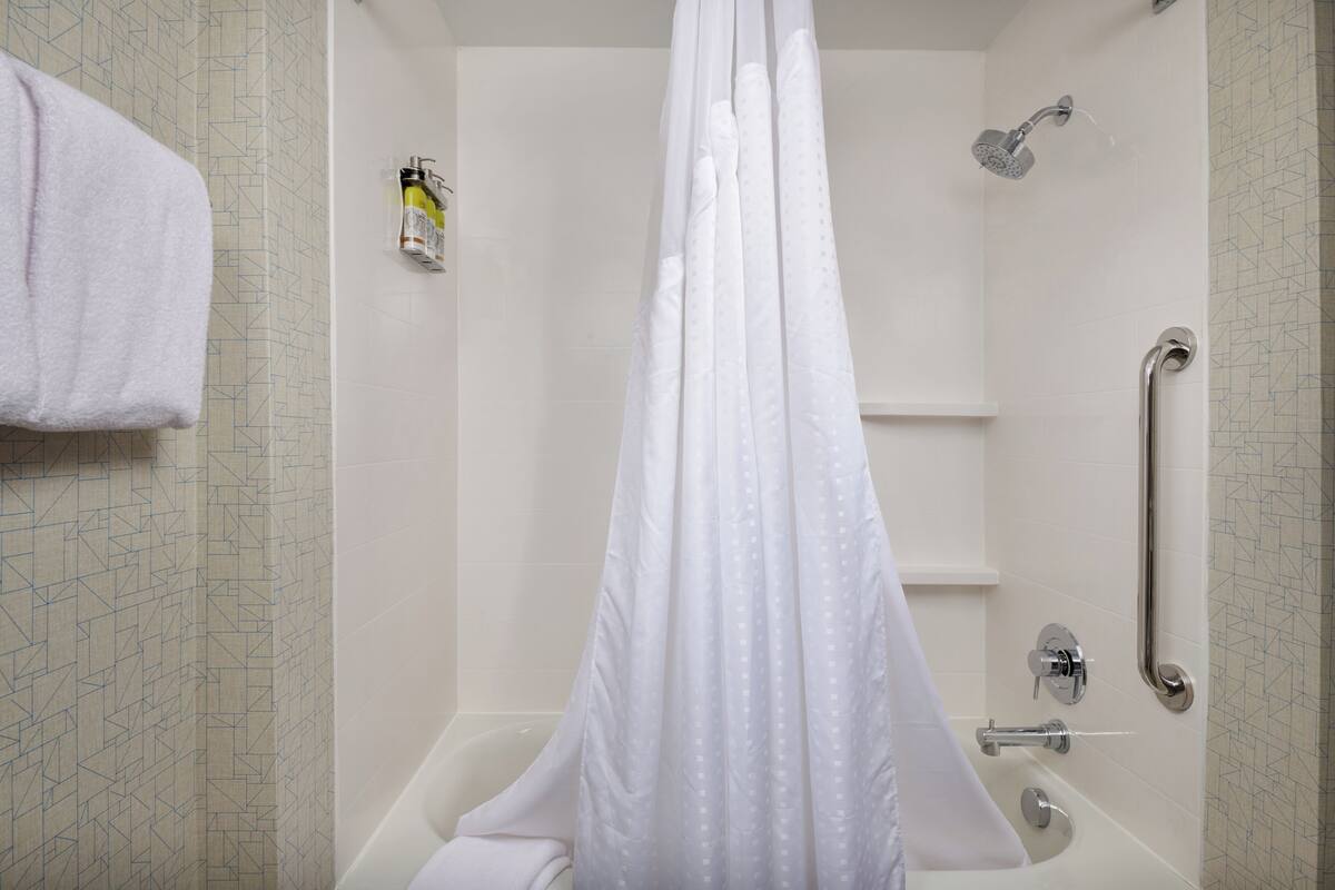Un baño moderno con ducha, un pasamanos y una botella de champú en la pared.