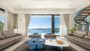 A modern living room with a large window, two sofas, a coffee table, and a staircase. - Luxury Villa Princess of Hvar with Pool (Hvar)