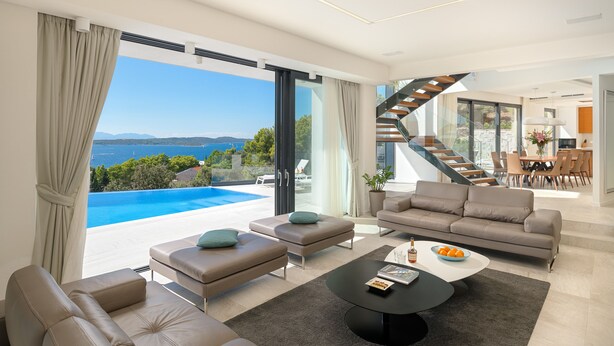 A modern living room with a large window overlooking a pool and the sea, a staircase, and a dining area. - Luxury Villa Princess of Hvar with Pool (Hvar)