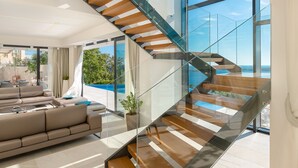 A modern living room with a large sofa, a glass staircase, and a view of the ocean. - Luxury Villa Princess of Hvar with Pool (Hvar)