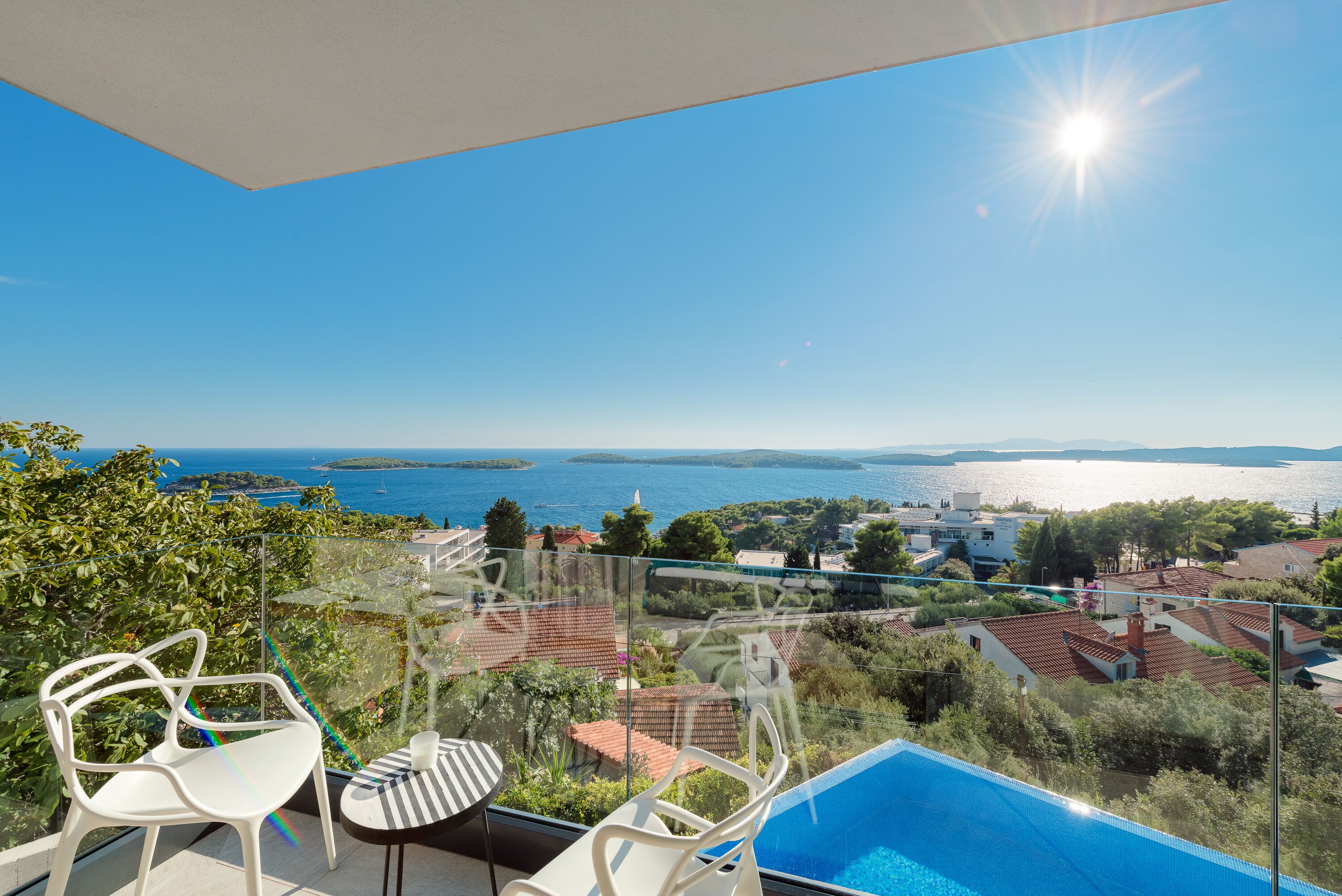 A balcony with a clear view of the sea, a swimming pool, and a glass railing.