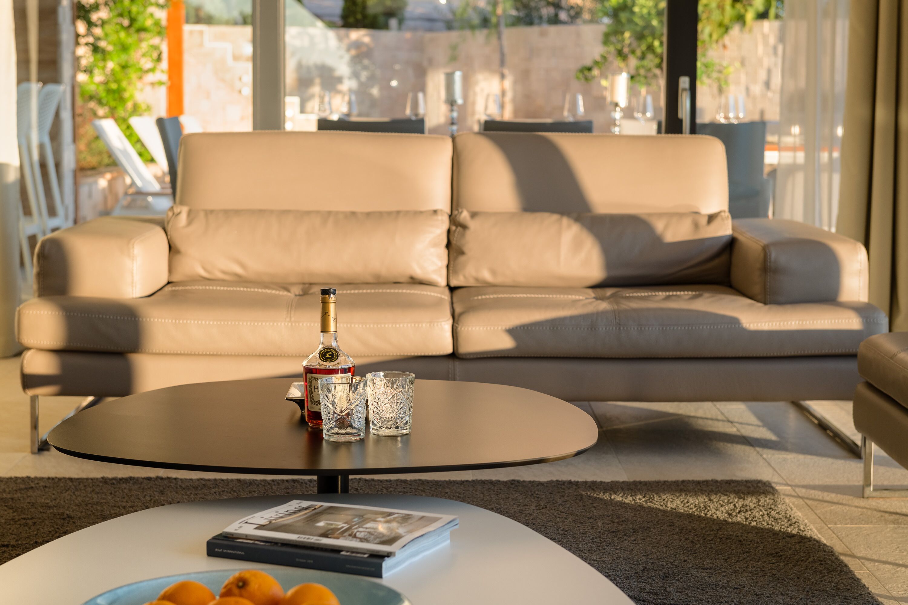 A modern living room with a beige leather sofa, a round coffee table, and a glass of red wine.