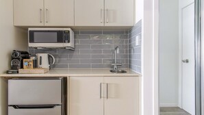 A compact kitchen with a microwave, coffee maker, kettle, and a small refrigerator. - Coastal Luxe 2BR Apartment + Spa Studio with Lagoo (PORT DOUGLAS)