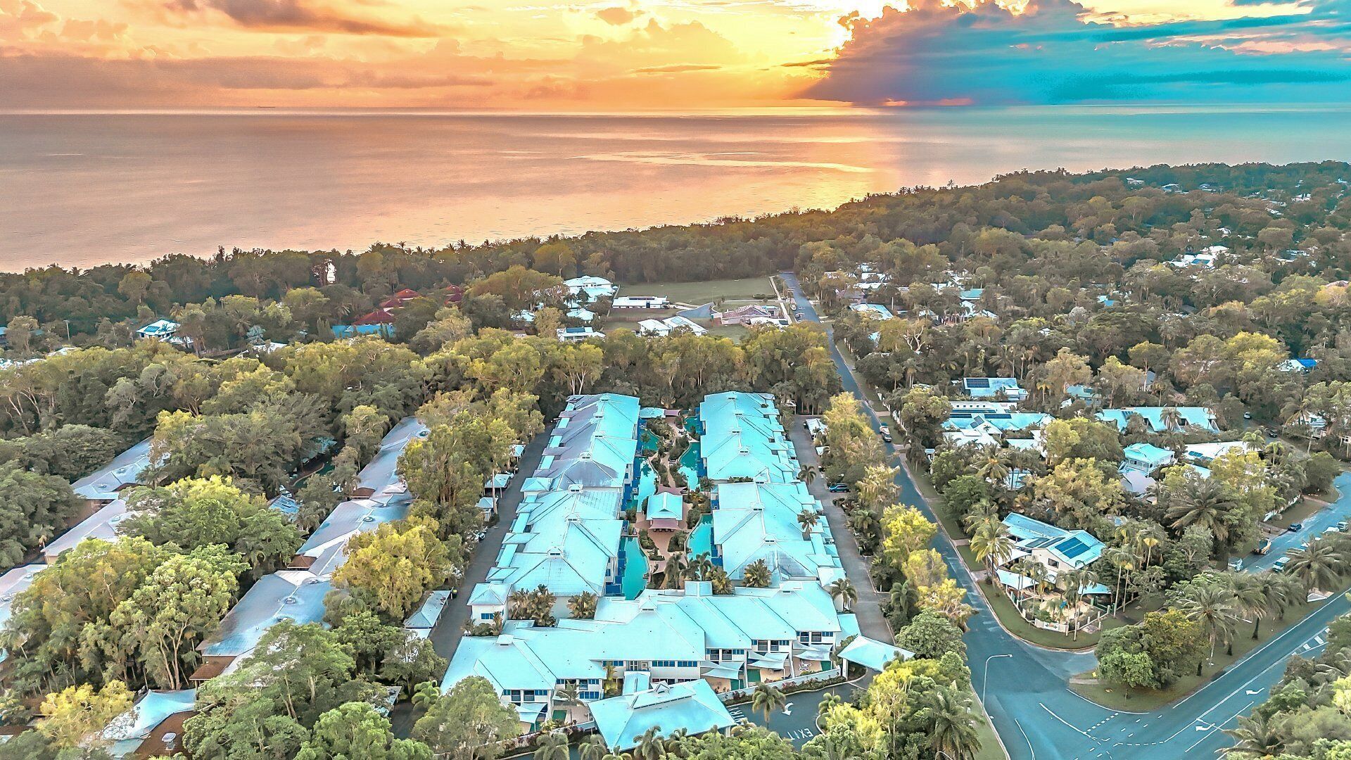 An aerial view of a resort with multiple buildings, a central swimming pool, and a surrounding forested area.