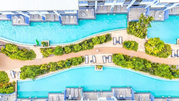 An aerial view of a hotel with multiple swimming pools, sun loungers, and lush greenery. - Coastal Luxe 2BR Apartment + Spa Studio with Lagoo (PORT DOUGLAS)