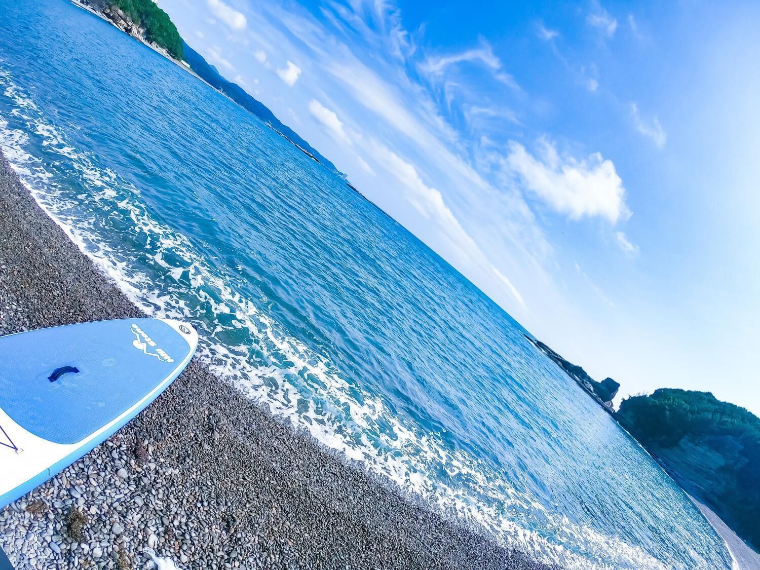 A beach with a surfboard and rocky shoreline.