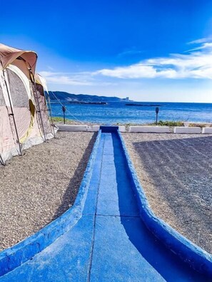 Zona de càmping amb una tenda i un camí blau que condueix a la mar.