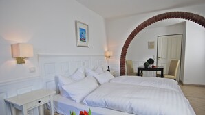 A hotel room with a large bed, a nightstand, a desk, and a chair. There is a brick archway leading to another room. - Nordseehotel Hörn van Diek (Esens)