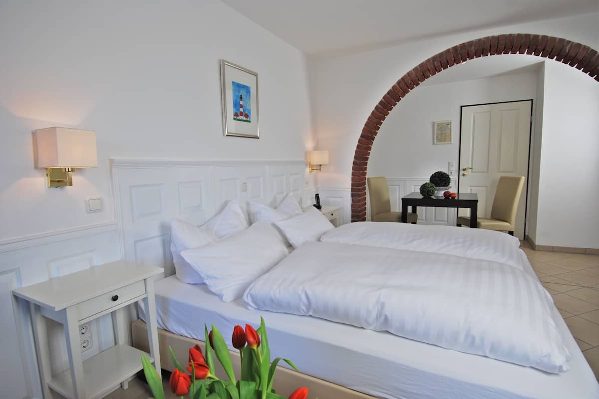 Habitación de hotel con una cama grande, una mesita de noche, un escritorio y una silla. Se ve un arco de ladrillo que conduce a otra habitación.