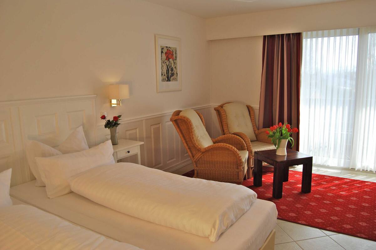 Una habitación de hotel con una cama grande, dos sillas, una mesita y un jarrón con flores.