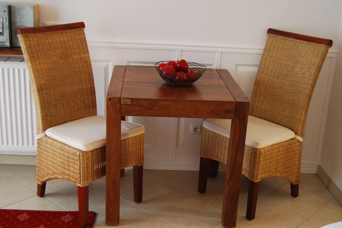 Una mesa de comedor con dos sillas de mimbre y un cuenco de fruta.