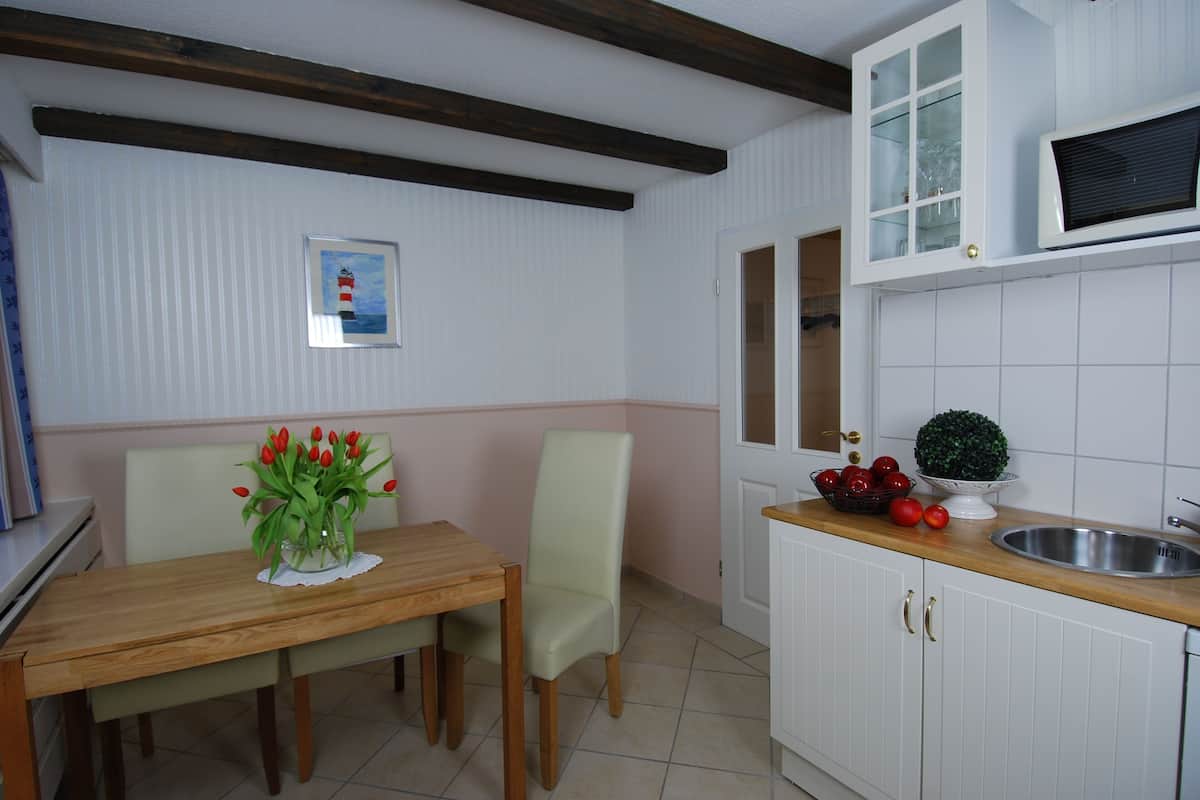 Un comedor con una mesa de madera, dos sillas, un jarrón de tulipanes y un cuadro en la pared.