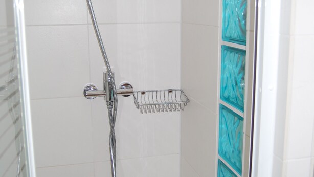 Ducha con grifería cromada, puerta de cristal y pared de azulejos blancos.