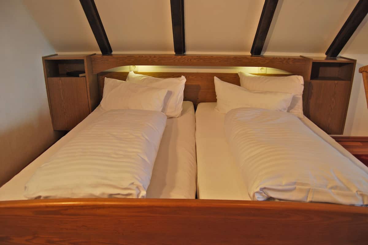 Una cama doble con cabecera de madera y mesitas de noche, en una habitación con techos inclinados y vigas a la vista.