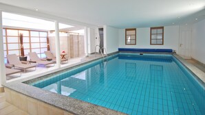 An indoor swimming pool with tiled walls, a blue pool, and lounge chairs. - Nordseehotel Hörn van Diek (Esens)